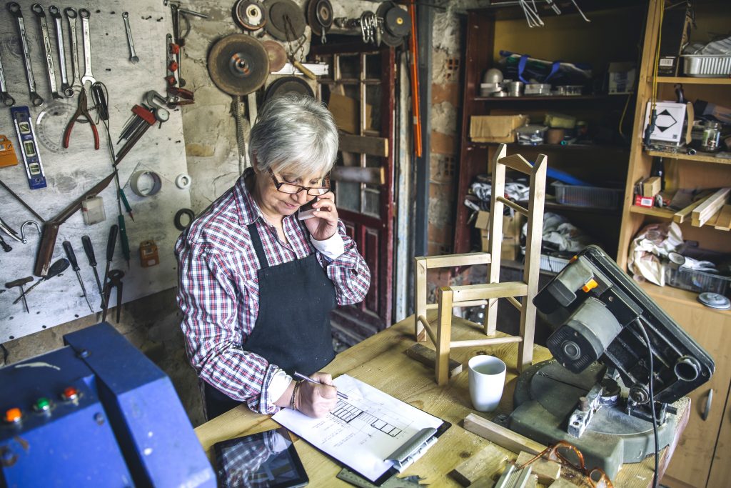 Frau telefoniert in einer Werkstatt und erfasst Inventar für den Verkauf von gebrauchtem Inventar